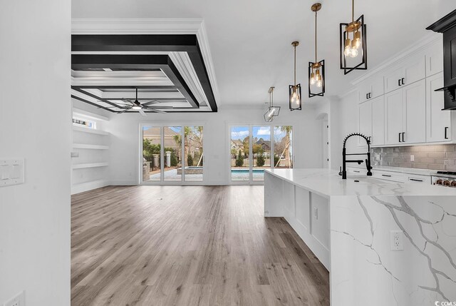 kitchen featuring pendant lighting, white cabinetry, backsplash, ornamental molding, and light stone countertops