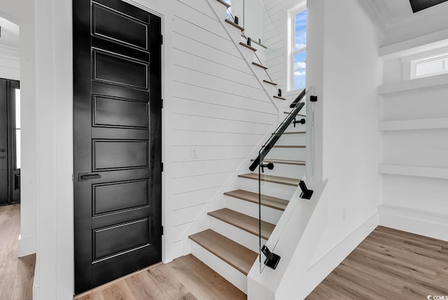 staircase with wood-type flooring and crown molding