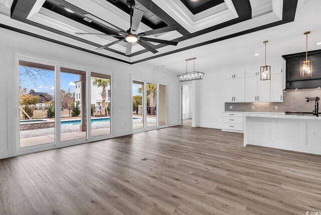 unfurnished living room featuring sink, ornamental molding, a tray ceiling, hardwood / wood-style flooring, and ceiling fan with notable chandelier