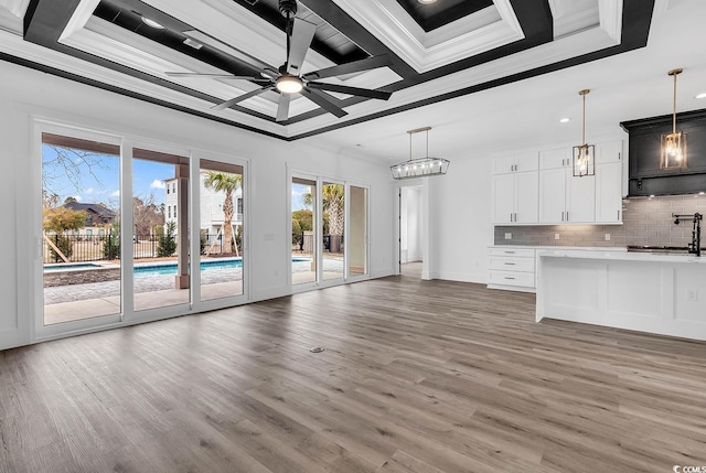 unfurnished living room with sink, hardwood / wood-style flooring, ornamental molding, ceiling fan with notable chandelier, and a raised ceiling