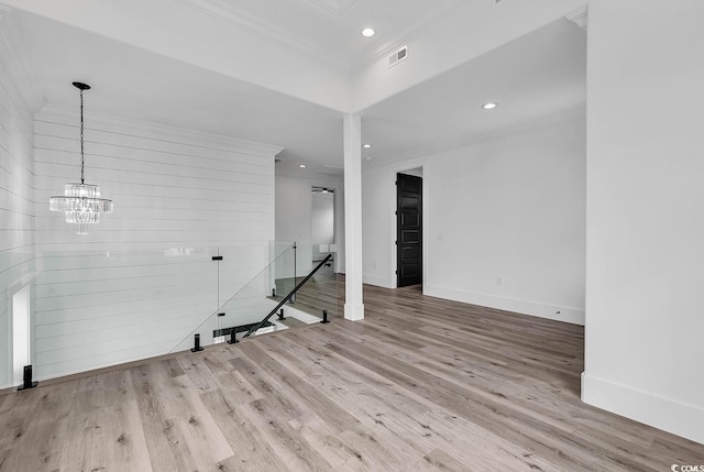 spare room featuring crown molding, wooden walls, an inviting chandelier, and light hardwood / wood-style flooring