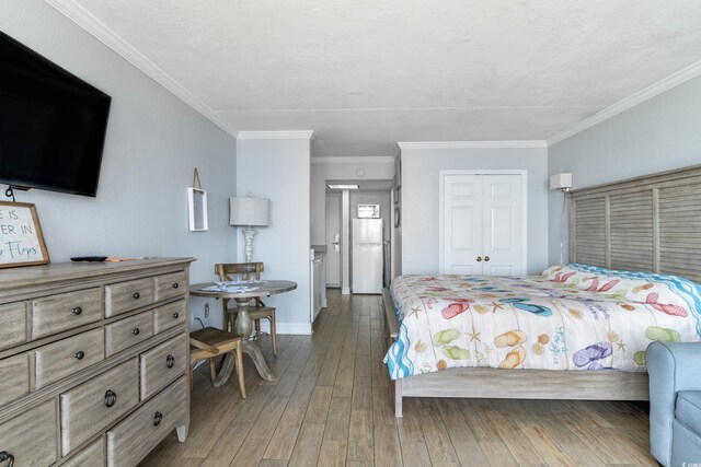 bedroom with a closet, crown molding, white fridge, and hardwood / wood-style flooring