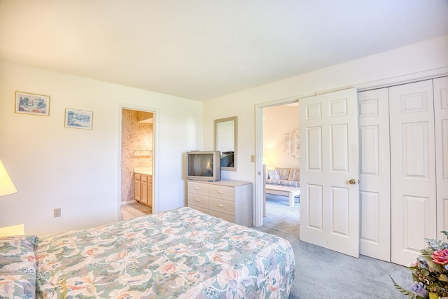 bedroom with a closet, light colored carpet, and ensuite bath