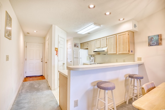 kitchen featuring light brown cabinets, a textured ceiling, light colored carpet, a kitchen breakfast bar, and white fridge