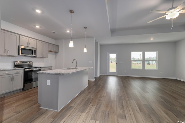 kitchen with light stone counters, stainless steel appliances, a kitchen island with sink, sink, and hardwood / wood-style floors