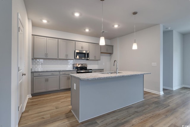 kitchen featuring pendant lighting, an island with sink, appliances with stainless steel finishes, and light hardwood / wood-style flooring