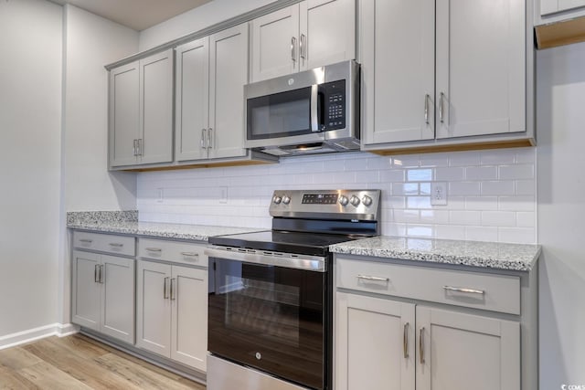 kitchen featuring light stone countertops, backsplash, light hardwood / wood-style floors, gray cabinets, and appliances with stainless steel finishes