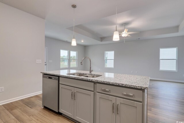 kitchen with light wood-type flooring, sink, dishwasher, hanging light fixtures, and an island with sink