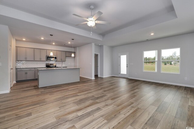 kitchen with gray cabinetry, pendant lighting, a kitchen island with sink, light hardwood / wood-style floors, and stainless steel appliances