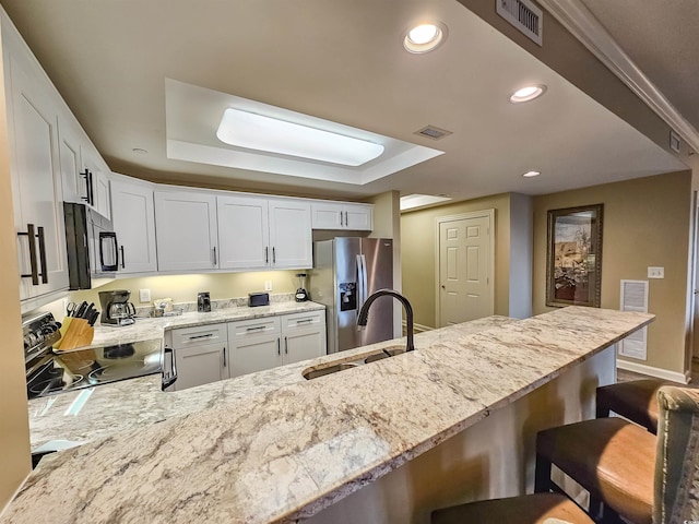 kitchen featuring black appliances, sink, white cabinets, a kitchen bar, and a tray ceiling