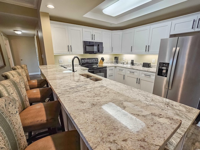 kitchen featuring light stone countertops, black appliances, white cabinets, and a kitchen bar