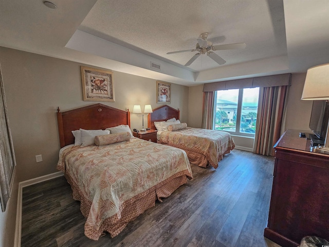 bedroom with dark hardwood / wood-style floors, ceiling fan, a tray ceiling, and a textured ceiling