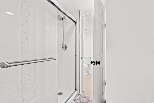 bathroom with hardwood / wood-style flooring, toilet, and a shower with shower door