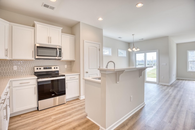 kitchen featuring a center island with sink, stainless steel appliances, light countertops, hanging light fixtures, and white cabinetry