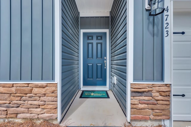 doorway to property with stone siding, board and batten siding, and a garage