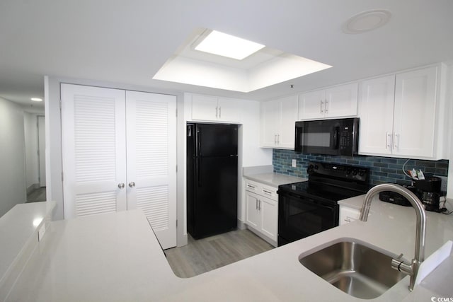 kitchen with black appliances, white cabinets, a raised ceiling, sink, and decorative backsplash