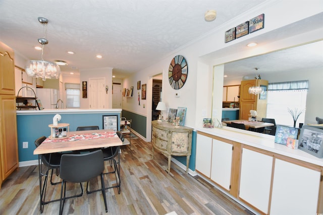 dining area featuring light wood-type flooring, a chandelier, crown molding, and a textured ceiling