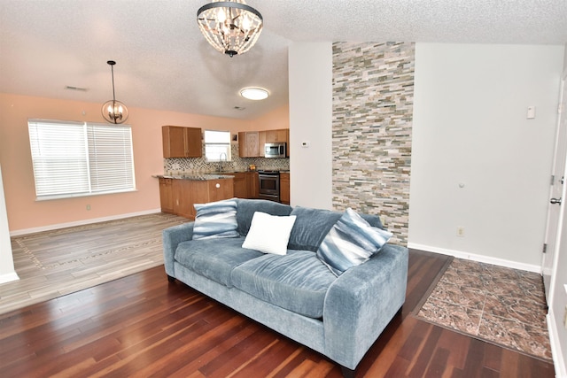 living room featuring dark wood-type flooring, lofted ceiling, a textured ceiling, and an inviting chandelier