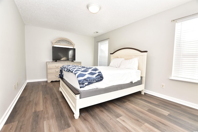 bedroom featuring a textured ceiling, baseboards, dark wood-style flooring, and multiple windows