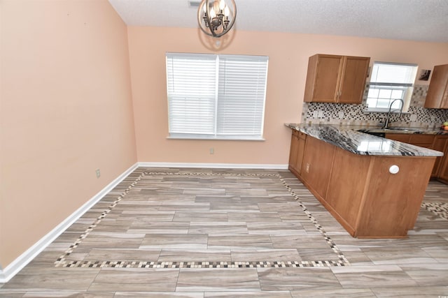 kitchen featuring decorative backsplash, brown cabinetry, a sink, dark stone countertops, and baseboards