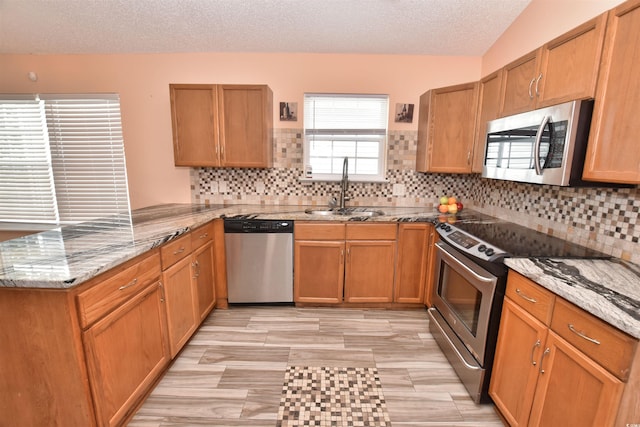 kitchen featuring appliances with stainless steel finishes, light stone counters, a peninsula, a textured ceiling, and a sink