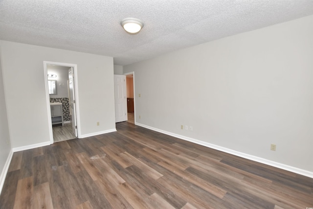 unfurnished bedroom with ensuite bath, a textured ceiling, baseboards, and dark wood-type flooring