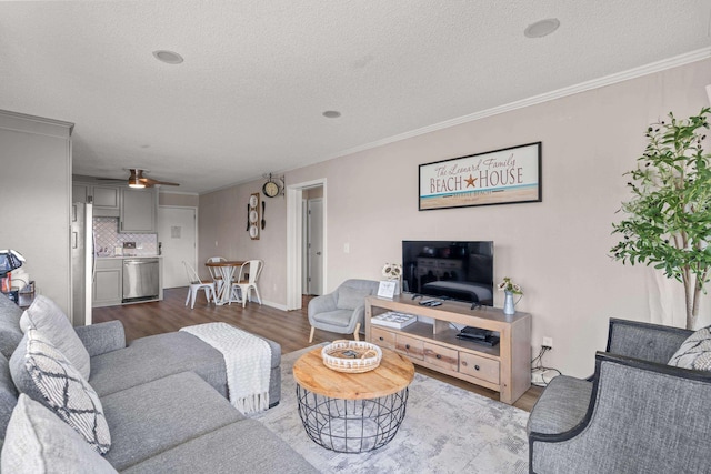 living area with a ceiling fan, crown molding, a textured ceiling, and wood finished floors