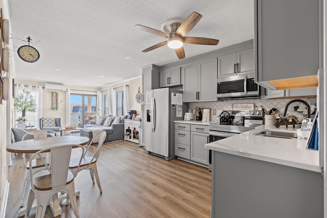 kitchen featuring open floor plan, stainless steel appliances, a sink, and gray cabinetry