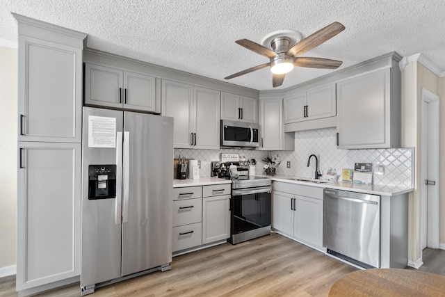 kitchen featuring light wood finished floors, tasteful backsplash, light countertops, appliances with stainless steel finishes, and a sink