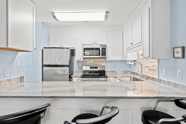 kitchen with white cabinets, a kitchen bar, light stone countertops, sink, and stainless steel appliances