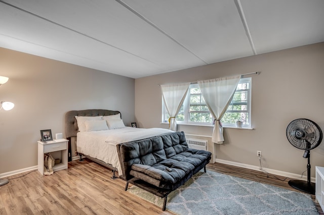 bedroom with baseboards, wood finished floors, and a wall mounted AC