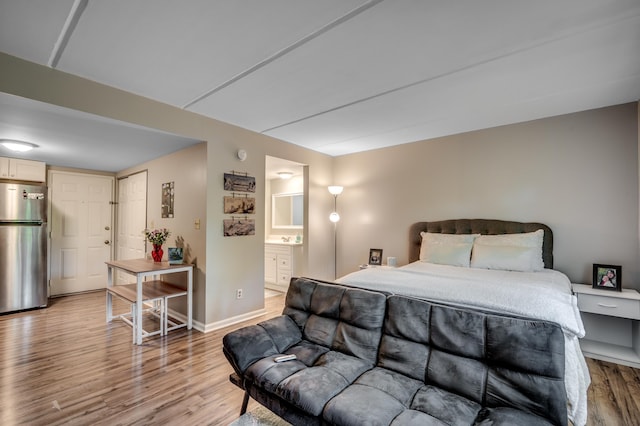 bedroom with freestanding refrigerator, baseboards, ensuite bath, and light wood finished floors