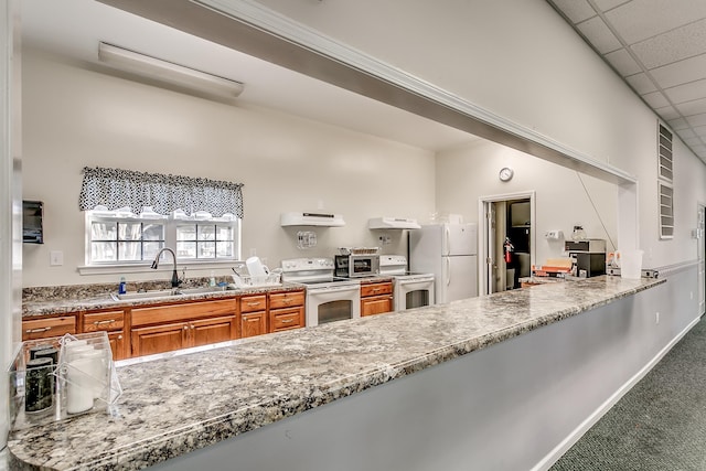 kitchen with carpet, brown cabinets, a sink, white appliances, and under cabinet range hood