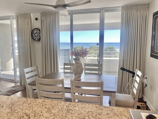 dining area with expansive windows, wood-type flooring, a water view, and ceiling fan