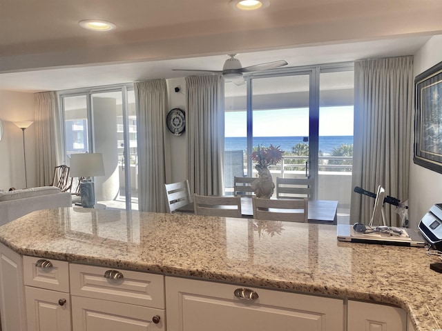 kitchen with light stone counters, ceiling fan, white cabinets, and a water view