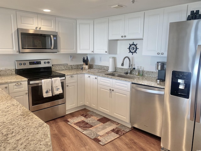 kitchen with sink, hardwood / wood-style flooring, appliances with stainless steel finishes, light stone countertops, and white cabinets