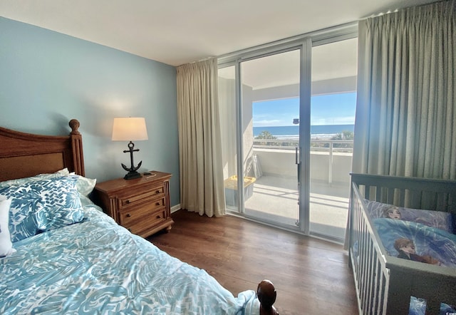 bedroom featuring hardwood / wood-style floors, a water view, access to outside, and a wall of windows