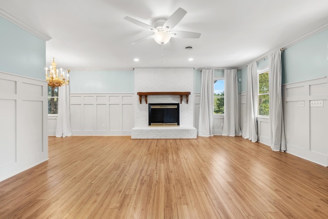 unfurnished living room featuring light wood-type flooring, ceiling fan with notable chandelier, a fireplace, and crown molding