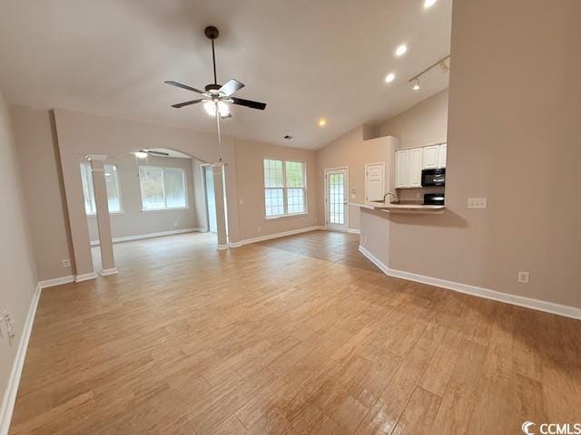 unfurnished living room featuring decorative columns, a healthy amount of sunlight, light wood-type flooring, and ceiling fan