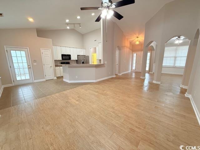 unfurnished living room with decorative columns, high vaulted ceiling, light wood-type flooring, and ceiling fan