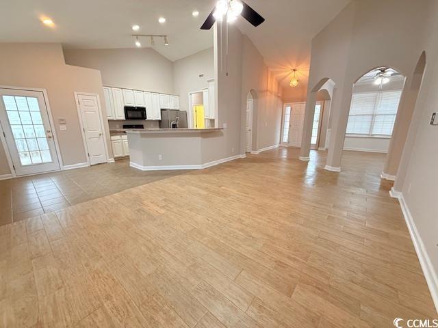 unfurnished living room featuring high vaulted ceiling, light wood-type flooring, and ceiling fan