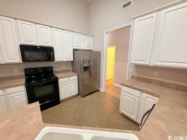 kitchen featuring light tile patterned flooring, white cabinets, and black appliances