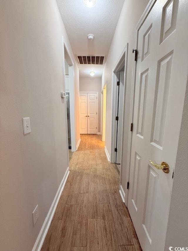 hallway featuring light hardwood / wood-style floors and a textured ceiling