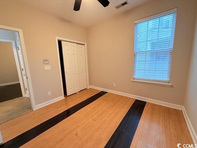 unfurnished bedroom featuring multiple windows, hardwood / wood-style floors, ceiling fan, and a closet