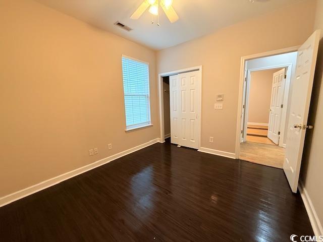 unfurnished bedroom with dark wood-type flooring, ceiling fan, and a closet