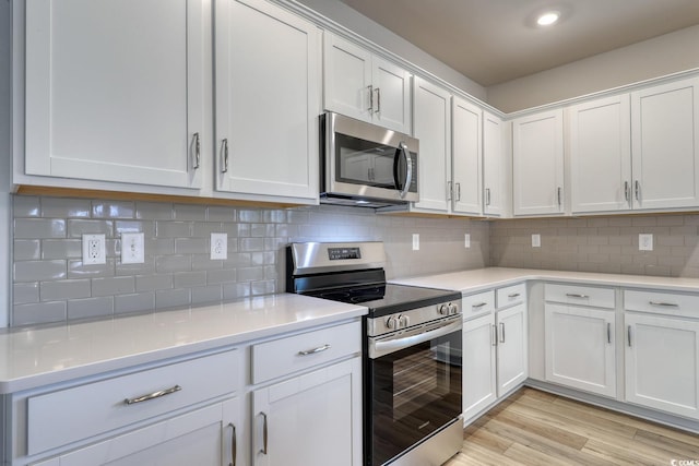 kitchen with white cabinets, stainless steel appliances, light hardwood / wood-style flooring, and tasteful backsplash