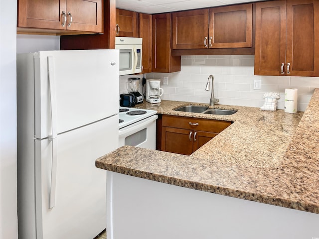 kitchen featuring light stone counters, backsplash, sink, and white appliances