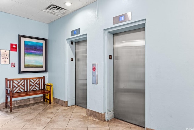 hallway featuring a paneled ceiling, light tile patterned flooring, and elevator