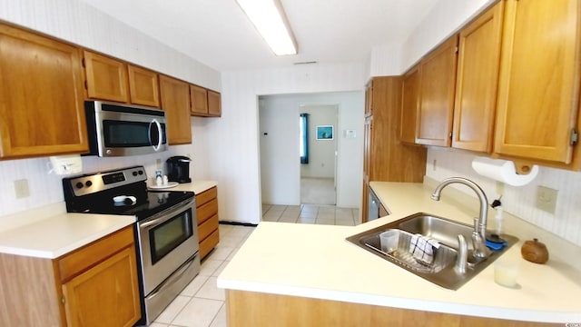 kitchen with appliances with stainless steel finishes, kitchen peninsula, sink, and light tile patterned floors