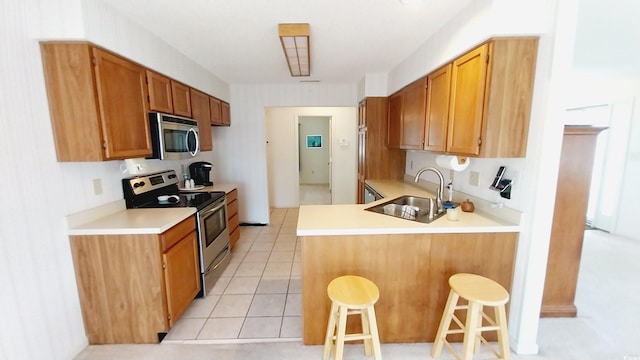 kitchen with sink, light tile patterned floors, kitchen peninsula, a breakfast bar area, and appliances with stainless steel finishes